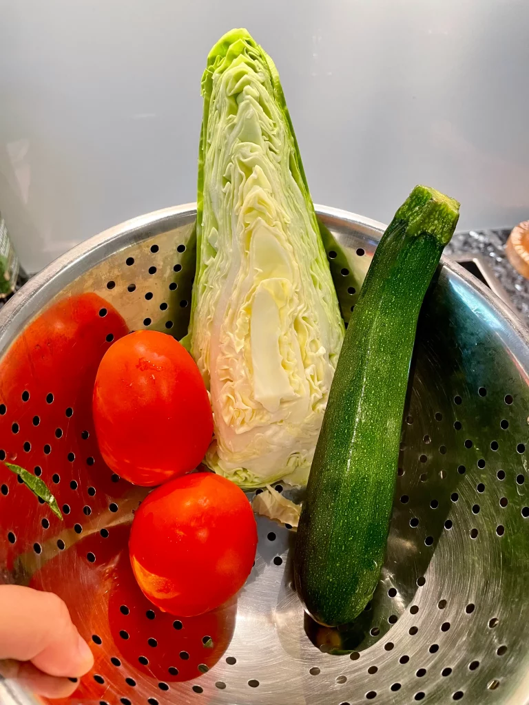 Fresh ingredients for sweetheart cabbage and courgette (zucchini) stir-fry on a kitchen counter: half a sweetheart cabbage, a courgette (zucchini), and two tomatoes.