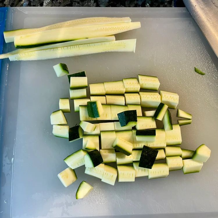 Courgette (zucchini) halved, seeded, and sliced into bite-sized pieces on a cutting board.