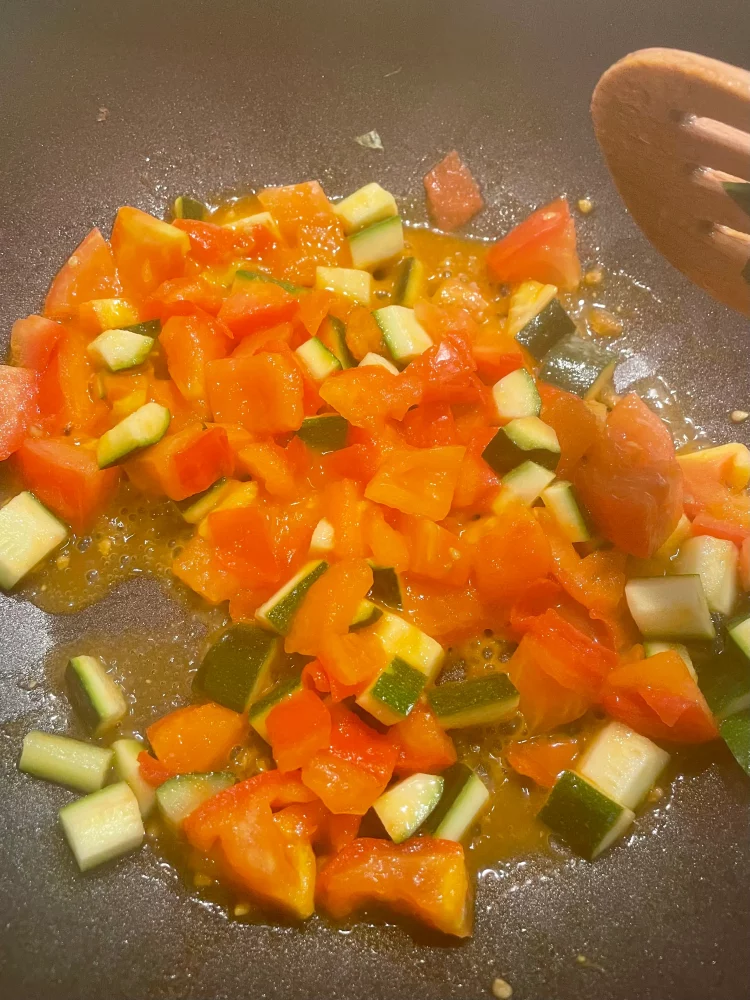 Chopped courgette (zucchini) and tomatoes simmering in a pan with sugar and salt seasoning.