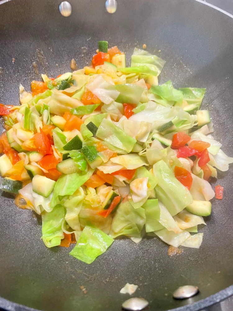 Cooked sweetheart cabbage being added back to the pan with courgette (zucchini) and tomatoes for final stir-frying.