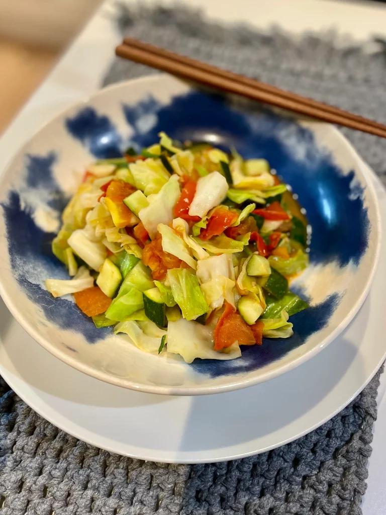 Close-up angled view of sweetheart cabbage, courgette (zucchini), and tomato stir-fry on a plate, showcasing vibrant colors and fresh textures.