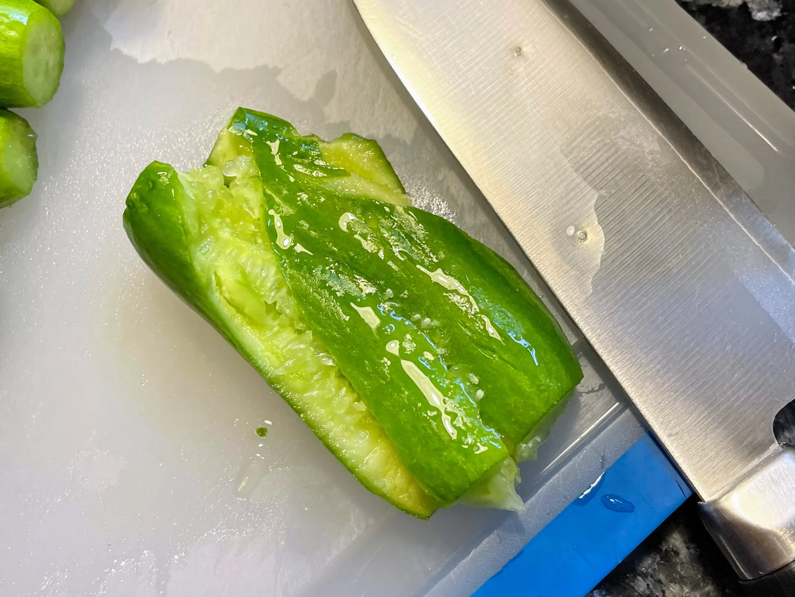 Baby cucumbers being pressed open with a knife, demonstrating a technique to enhance flavor absorption.