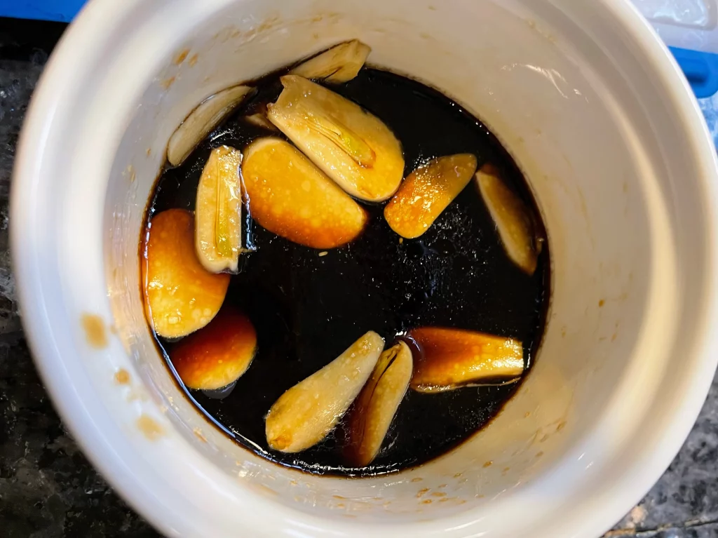 Garlic slices and chili in a bowl with soy sauce, black rice vinegar, sesame oil, and sugar, creating a savory dressing for the salad.