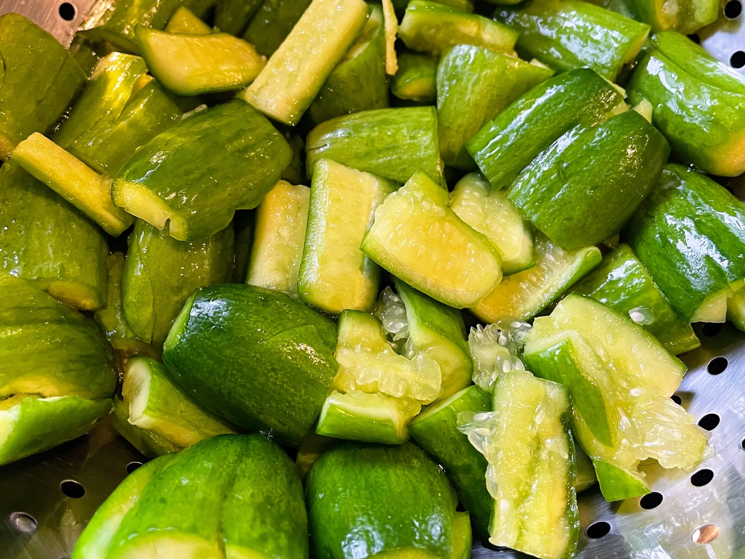 Prepared cucumbers in a mixing bowl with sauce poured over, ready to be combined for a flavorful dish.