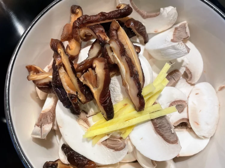 Julienned fresh ginger and rehydrated shiitake mushrooms placed on a cutting board after soaking.