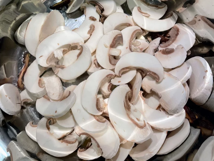 Fresh mushrooms, rehydrated shiitake mushrooms, and julienned ginger stir-frying in a pot with cooking oil over medium-high heat.