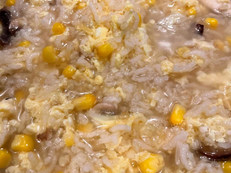 Simmering Chinese veggie congee in a pot, with rice becoming puffy and the mixture thick and creamy.