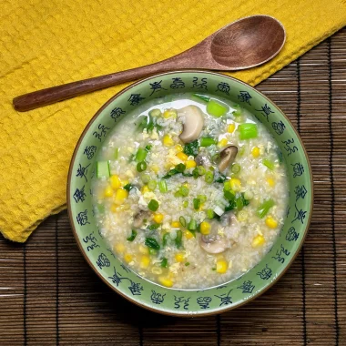 Finished Chinese veggie congee served in a bowl, garnished with chopped spring onions and a drizzle of sesame oil.