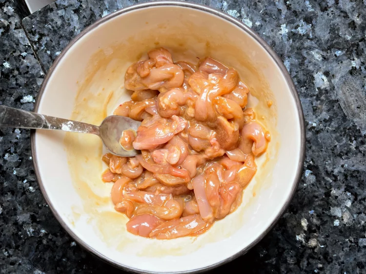 Marinated chicken strips in a bowl with soy sauce, sesame oil, sugar, and corn starch.