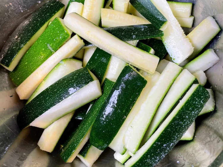 Salted courgette strips resting in a container to remove bitterness and retain crunch.