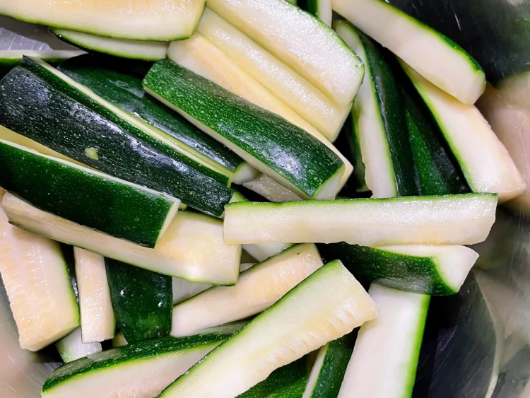 Salted courgette being washed under running water to remove excess salt and bitterness.