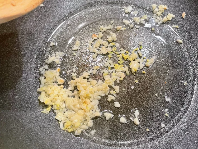 Minced garlic and ginger sizzling in a hot pan to release their aroma for the stir fry.