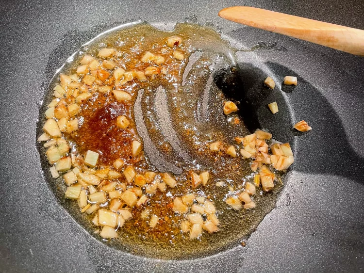 Sautéing minced garlic and Shacha sauce in a wok for beef stir-fry