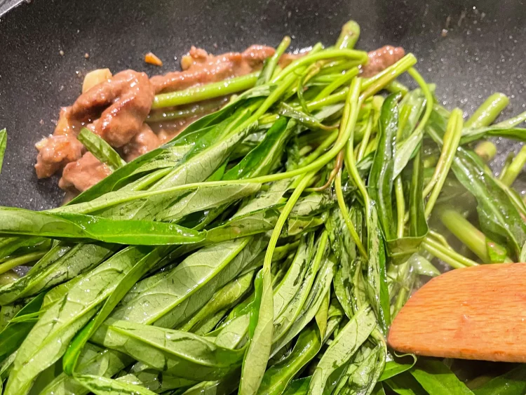 Finishing the dish by adding water spinach leaves to the wok